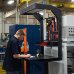 man working at an ergonomic sit stand workbench on manufacturing shop floor next to cnc machine